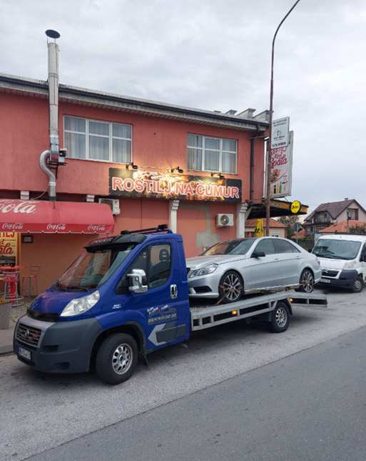 Šlep vozilo Nešo prevozi automobil ulicama grada pored lokalnih radnji
